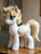 Size: 768x1024 | Tagged: safe, ai generated, generator:pony realism 2.2, oc, oc only, oc:swift songster, alicorn, pony, alicorn oc, female, folded wings, horn, indoors, irl, looking offscreen, mare, photo, plushie, smiling, solo, standing, table, wings